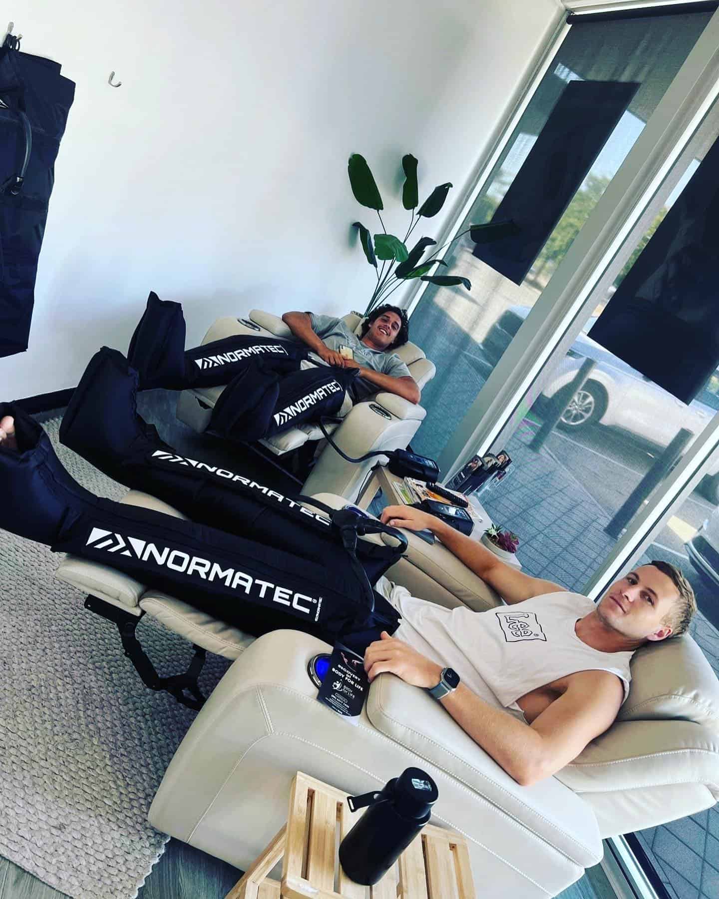 Two young men relaxing while using NormaTec compression boots